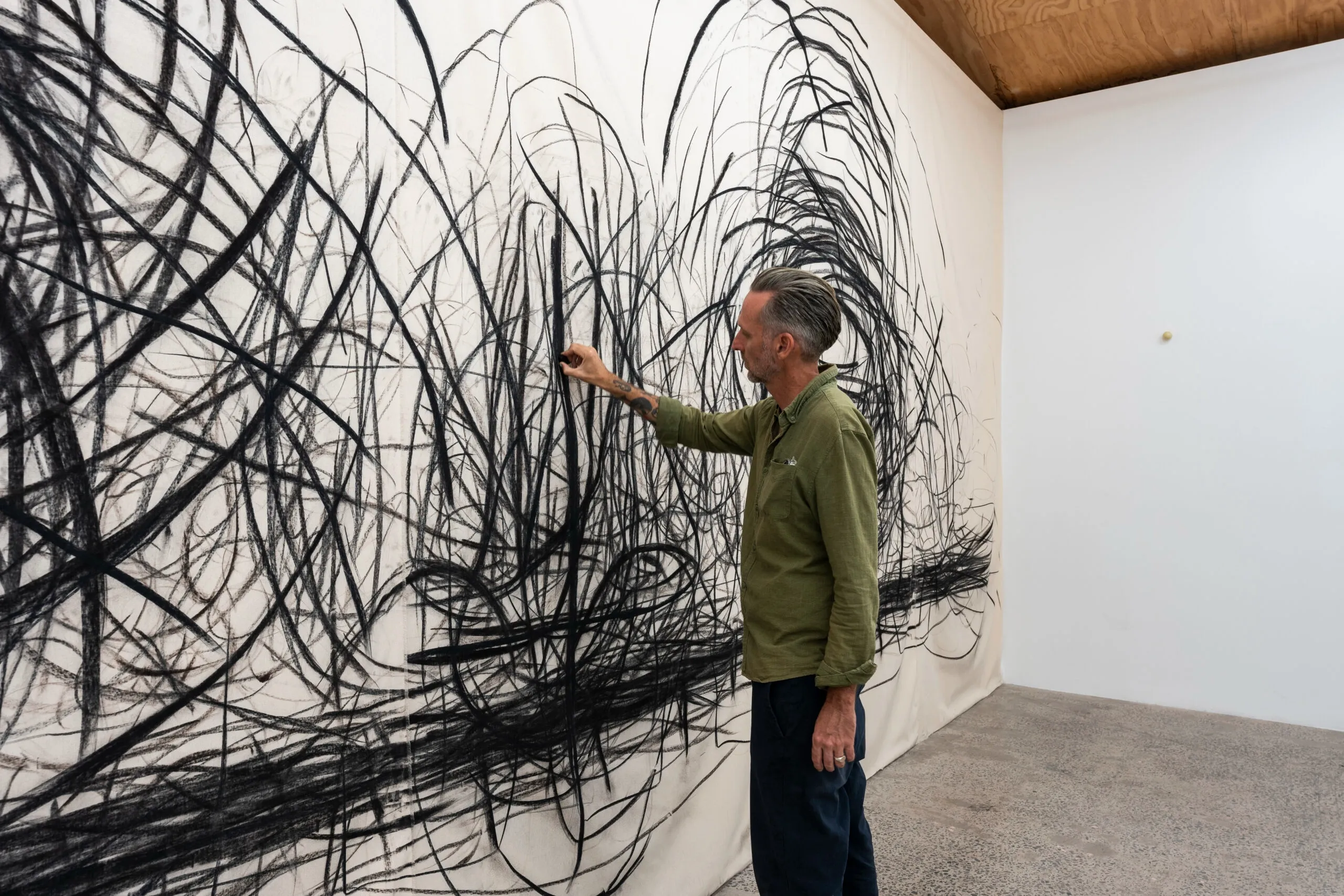 Laith McGregor drawing in charcoal across a large unstretched canvas hung in a gallery.